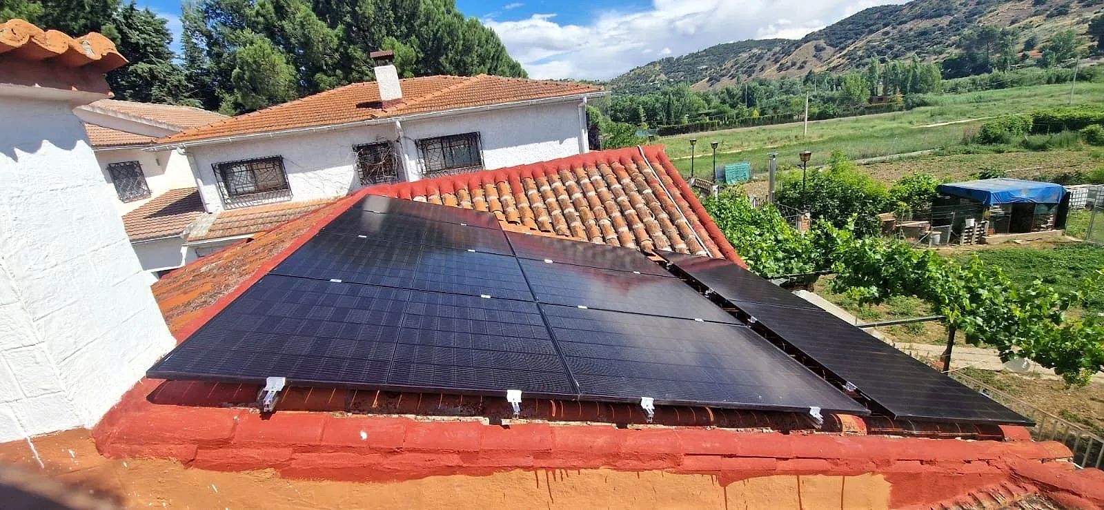 Paneles solares negros sobre un tejado de teja árabe con montañas y huertas al fondo