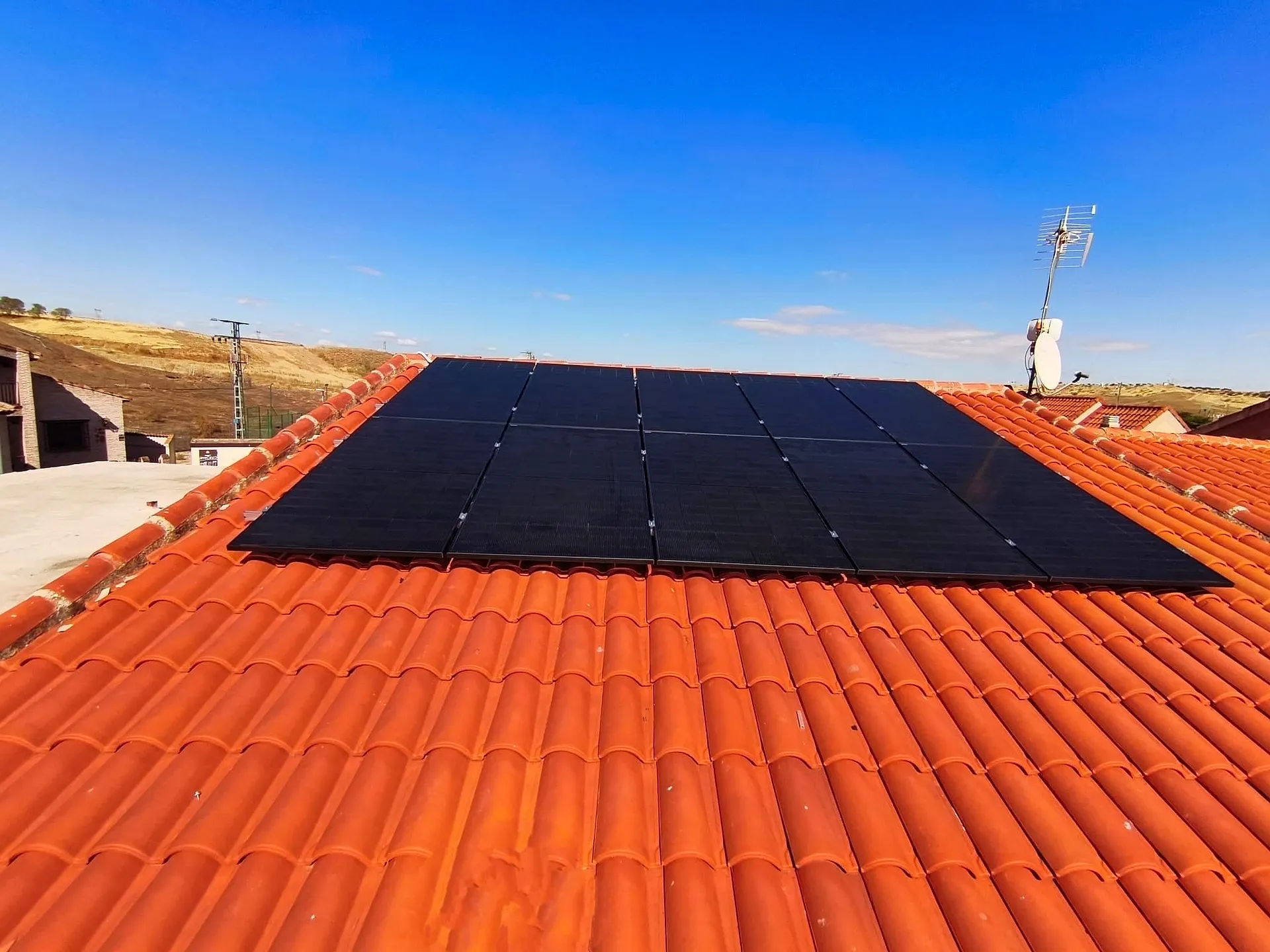Fila de diez paneles solares negros sobre un tejado de teja bajo el cielo despejado
