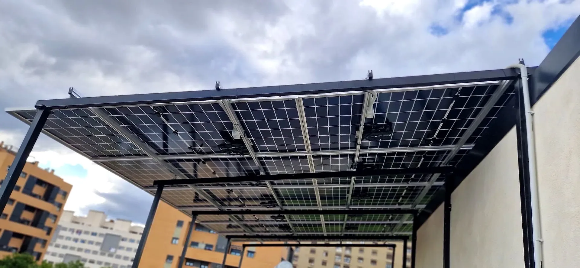 Pérgola fotovoltaica con estructura metálica vista desde abajo, con las células visibles a través del vidrio de los paneles
