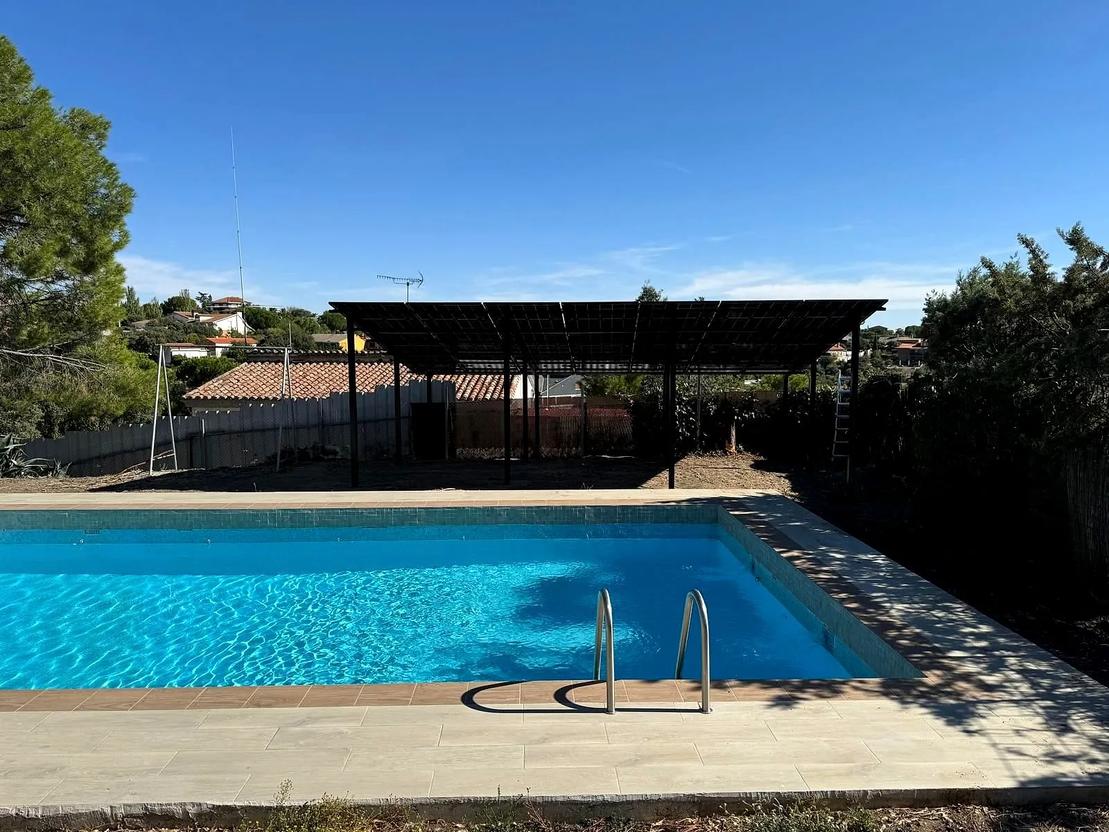 Pérgola con paneles solares en el jardín de una vivienda, junto a la piscina